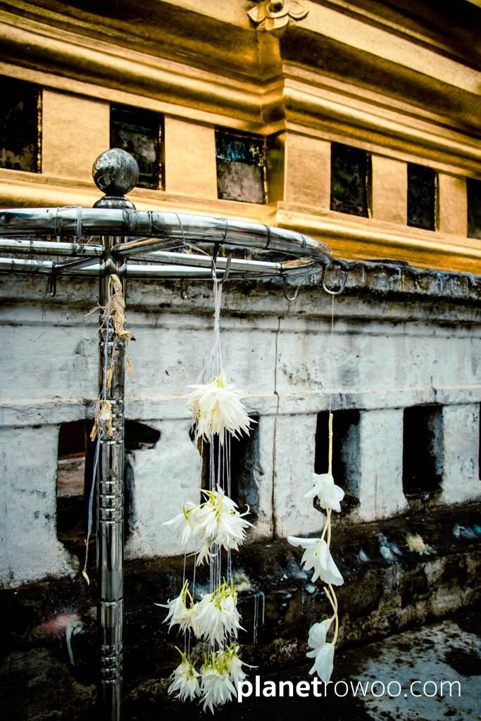 Temple offerings hang in front of remnants of the enamelled Jataka plaques at the Shwezigon Pagoda