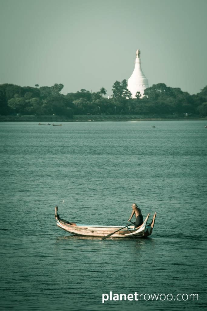 A local rows his boat in Taungthaman Lake with temple beyond