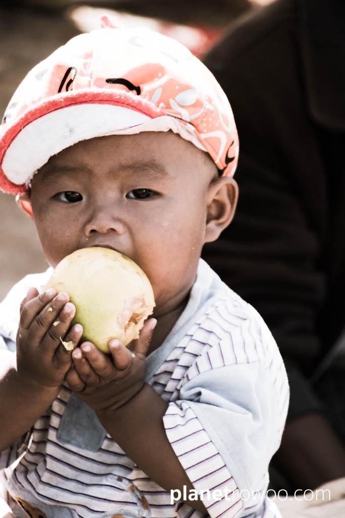 Small child eats large fruit at Kalaw market